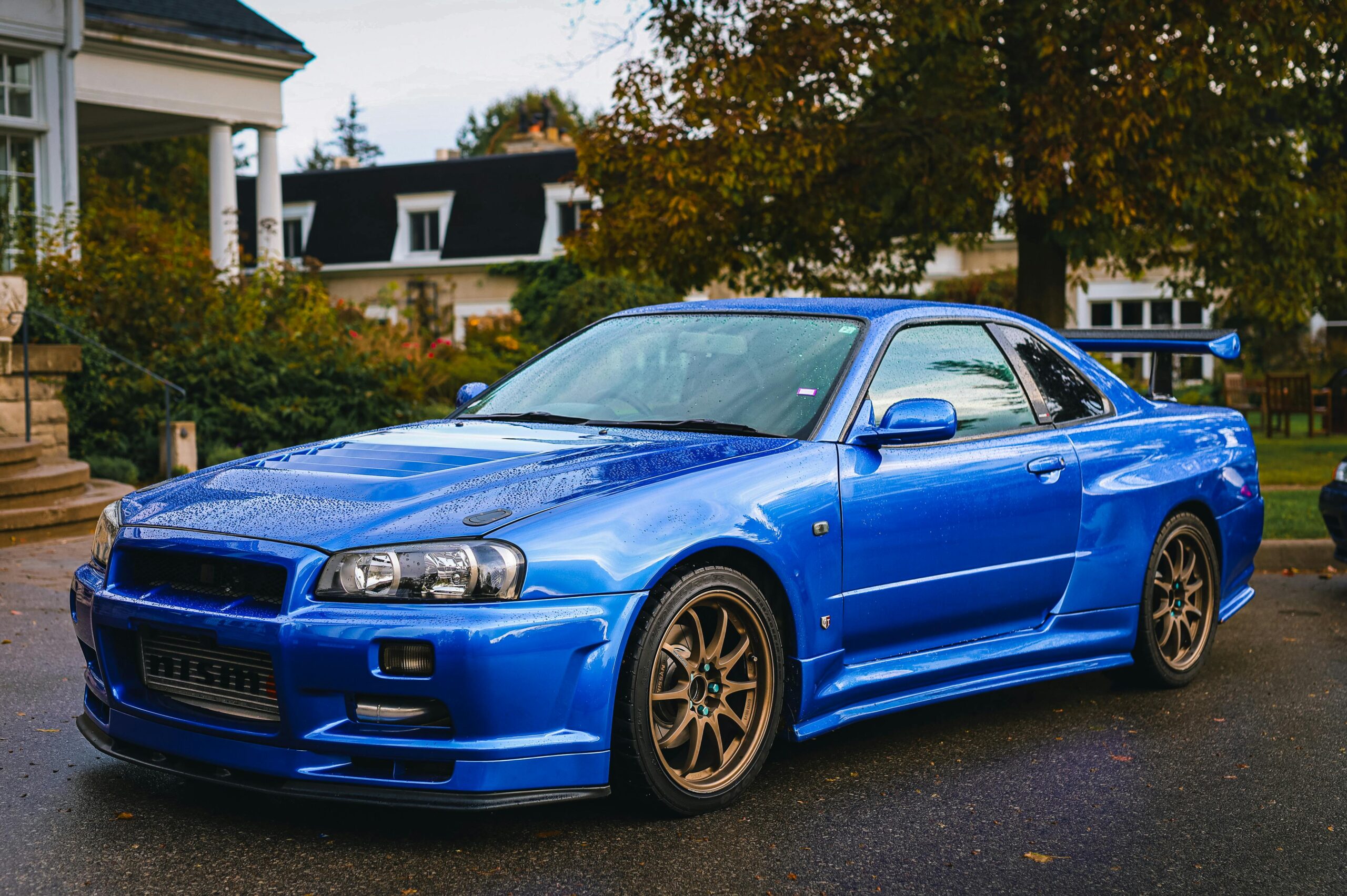 A stunning blue Nissan Skyline GT-R R34 parked in a residential area captured in a contemporary style.